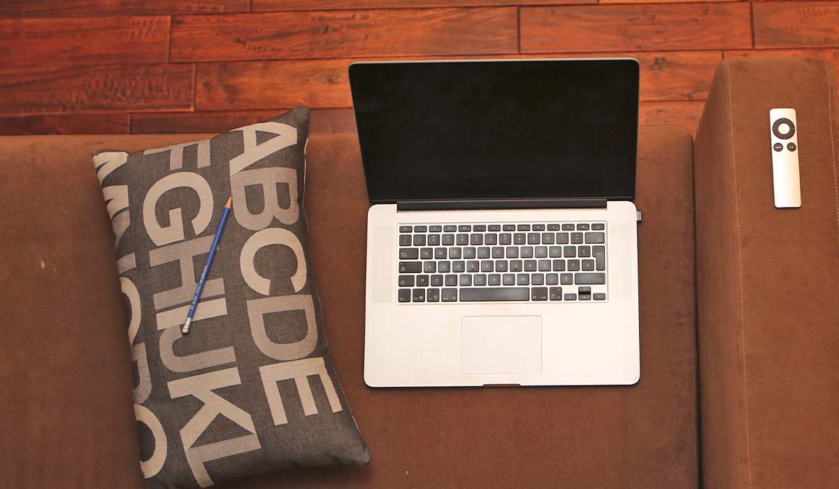 MacBook on a couch, Apple Tv remote and a letter pillow