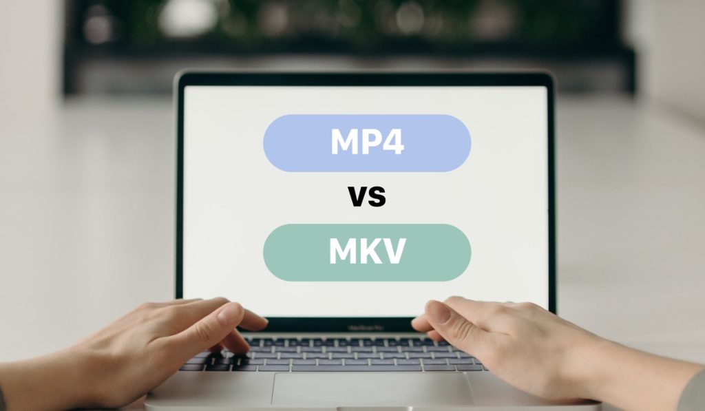Two hands using a MacBook on a white table. The MacBook screen shows two large buttons - a blue one with 'MP4' on the upper side and a red one with 'MKV' on the lower side. There's a 'VS' between them.